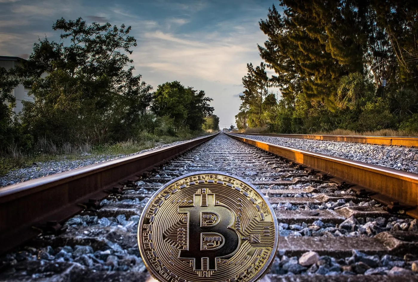 A physical Bitcoin coin resting on railway tracks, symbolising a long path to yield